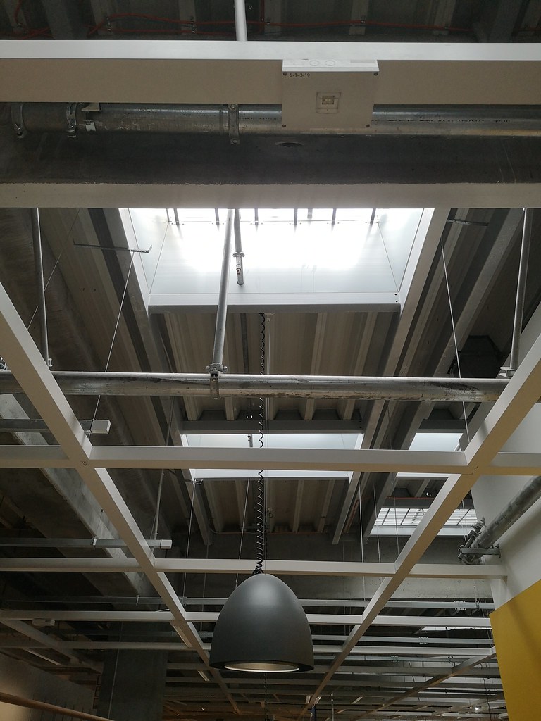 Unique architectural ceiling design featuring skylight and industrial light fixture in modern workspace