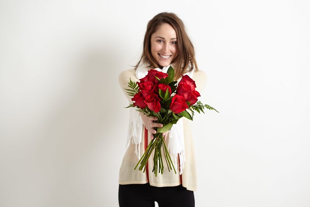 woman in white sweater and black pants with bouquet of red roses